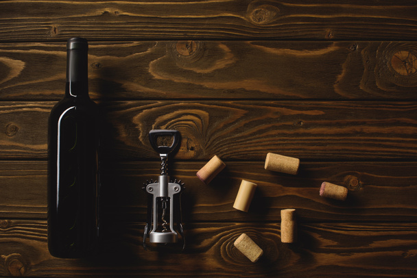 Draufsicht auf Flasche Luxus-Rotwein mit Korken und Korkenzieher auf Holztisch - Foto, Bild