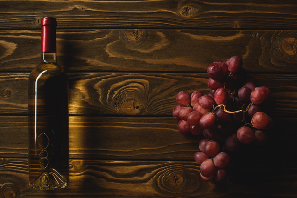κάτοψη του μπουκάλι λευκό κρασί και υποκατάστημα των σταφυλιών στο ξύλινο τραπέζι - Φωτογραφία, εικόνα