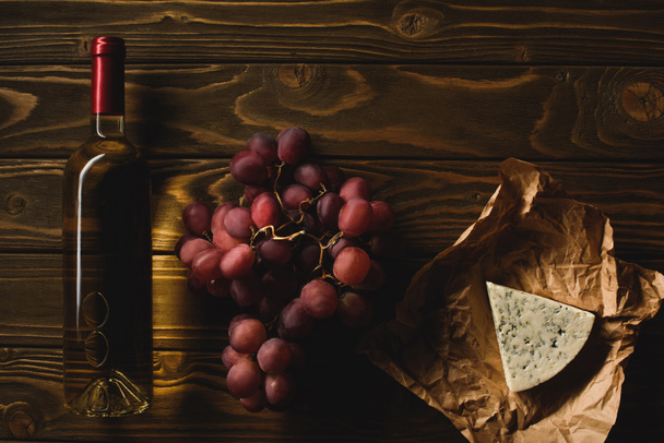 pohled shora na láhev bílého vína s předkrmy na dřevěný stůl - Fotografie, Obrázek