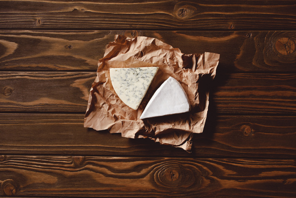 Widok z góry plasterki sera na zmięty papier na drewnianym stole - Zdjęcie, obraz