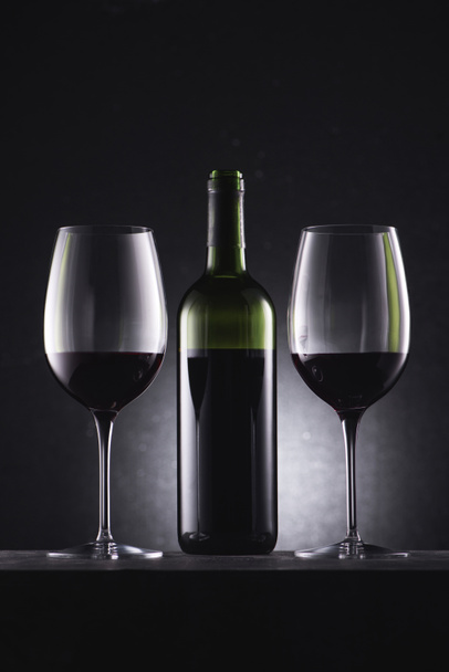 glasses filled with red wine and wine bottle in middle on black - Foto, Imagem