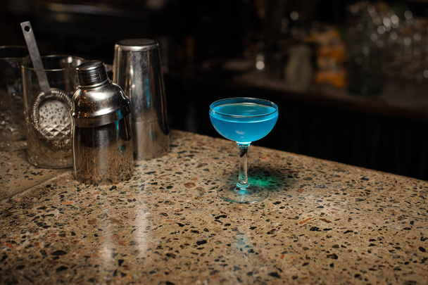 Алкогольный коктейль Голубая лагуна в стакане стоит на барной стойке
 - Фото, изображение