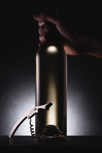cropped shot of man holding bottle of white wine on black with corkscrew - Foto, afbeelding