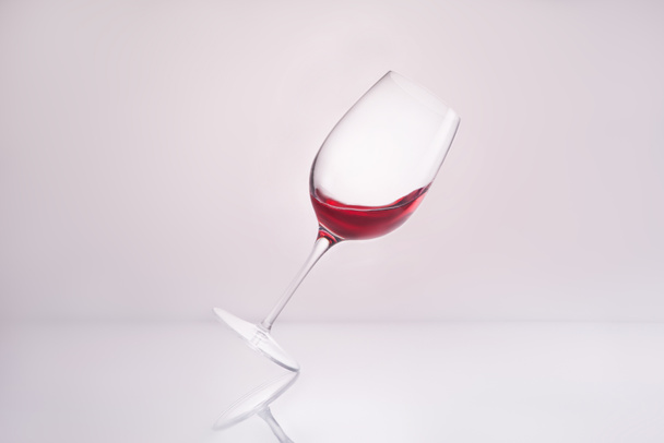 inclined wineglass with splashing luxury red wine on reflective surface and on white - Photo, Image