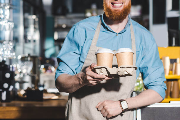 コーヒーの 2 つの使い捨てカップを保持している男性のバリスタの笑顔の画像をトリミング  - 写真・画像