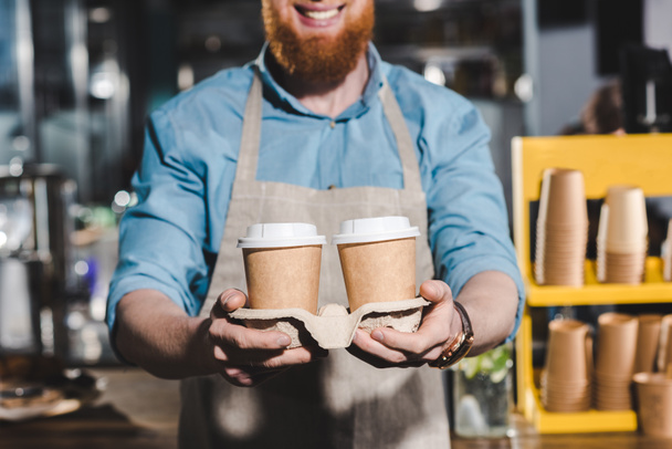 imagem cortada de sorrir barista masculino segurando duas xícaras descartáveis de café
  - Foto, Imagem