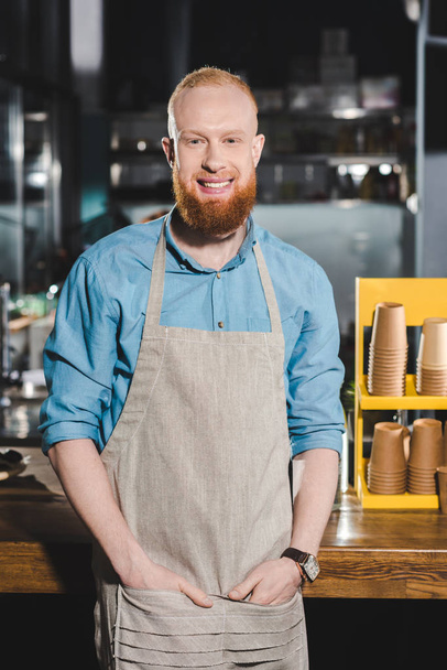 smiling young male barista in apron standing in coffee shop  - Фото, зображення