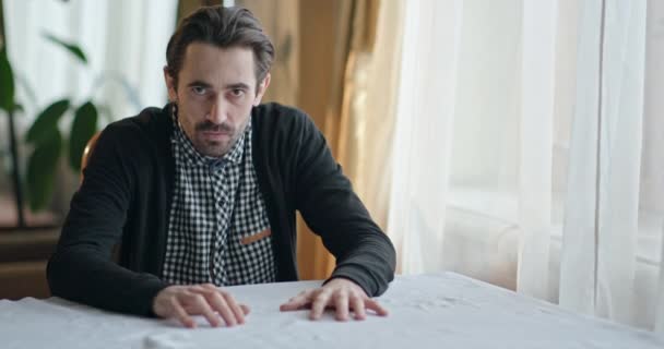 Emotional man sitting at a table at home, suddenly rising and ripping the cloth off the surface before sitting down with his head in his hands. - Materiał filmowy, wideo