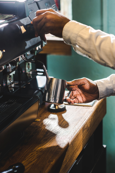 close-up partial view of african american barista making cappuccino at coffee machine - Photo, image