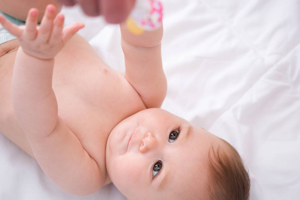 Imádnivaló baba kislány játszó cumi a fehér ágy - Fotó, kép