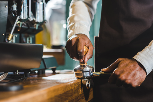 γκρο πλαν μερική άποψη του barista στην ποδιά προετοιμασία του καφέ στη καφετιέρα  - Φωτογραφία, εικόνα