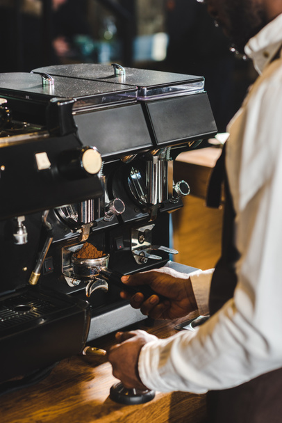Schnappschuss eines afrikanisch-amerikanischen Baristas in Schürze beim Zubereiten von Kaffee an der Kaffeemaschine - Foto, Bild