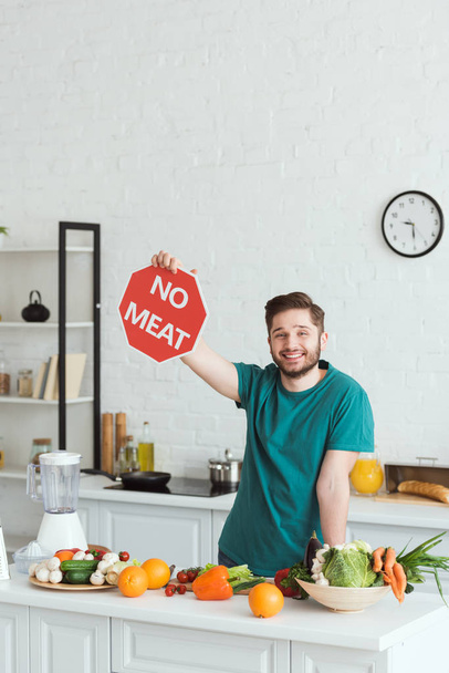lachende knappe vegan man met geen teken van vlees in de keuken - Foto, afbeelding