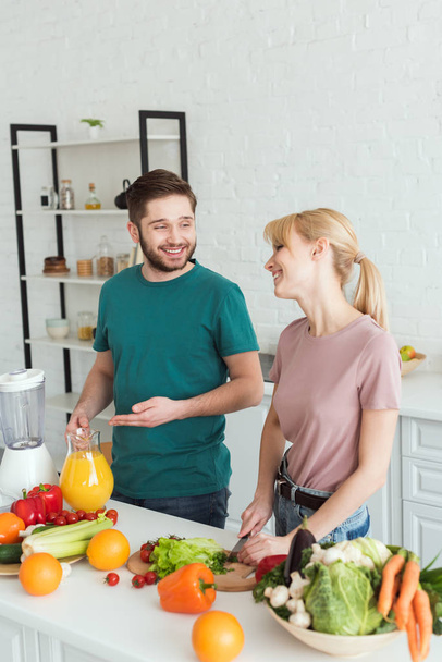 couple of vegans smiling and talking while cooking food at kitchen - Photo, Image