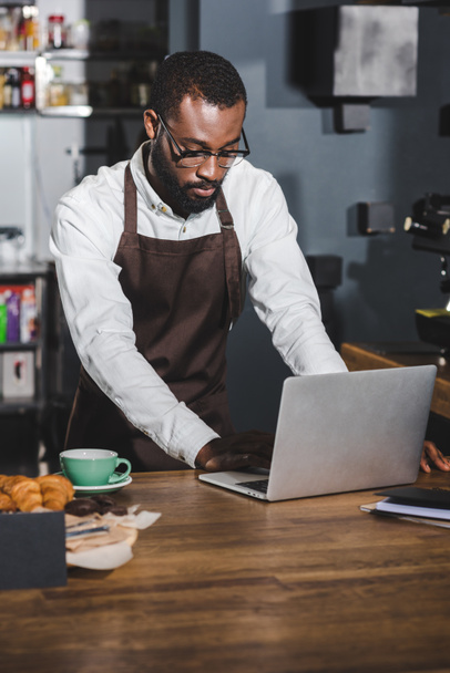 młody Afroamerykanin barista korzysta z laptopa podczas pracy w kawiarni - Zdjęcie, obraz