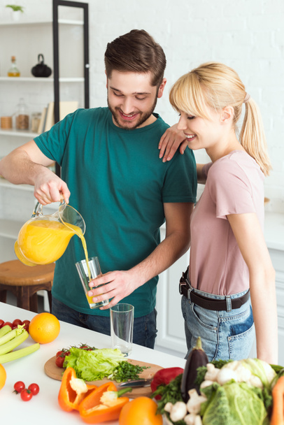 happy vegan boyfriend pouring fresh juice into glass in kitchen - Foto, immagini