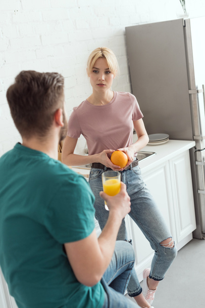 couple of vegans talking in kitchen and holding orange and orange juice - Photo, Image