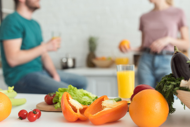 image recadrée de couple végétalien parlant dans la cuisine avec des fruits et légumes au premier plan
 - Photo, image