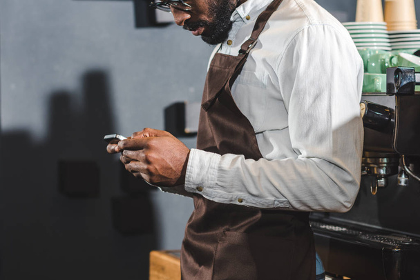 cropped shot of young african american bartender using smartphone - Fotó, kép