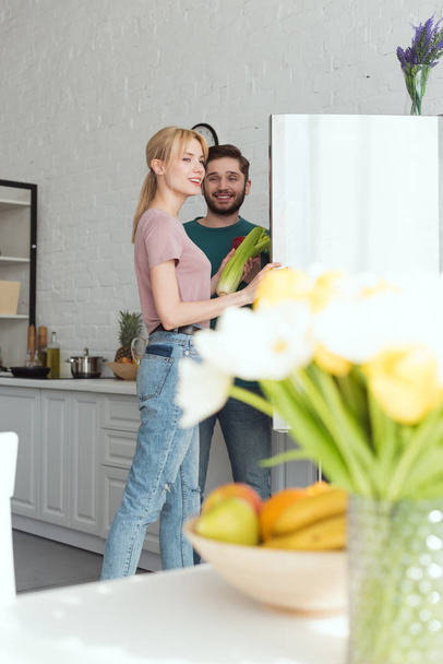 couple of vegetarians taking vegetables from fridge in kitchen - Photo, Image