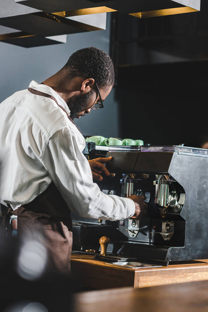 młody Afroamerykanin barista w okularach i fartuch pracę z ekspresem do kawy - Zdjęcie, obraz