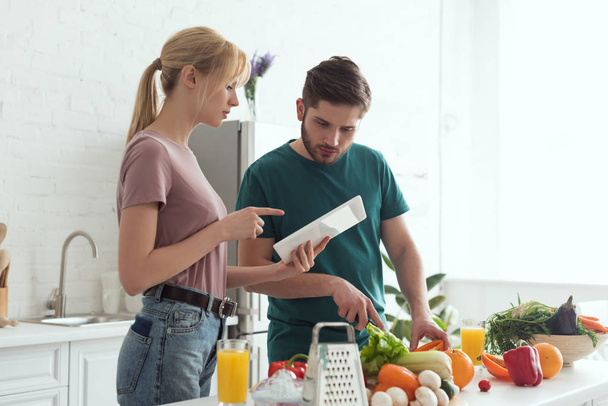girlfriend pointing on tablet with recipe during cooking at kitchen, vegan concept - Photo, Image