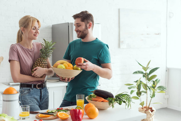 young vegan couple with fresh fruits and vegetables in kitchen at home - Photo, Image