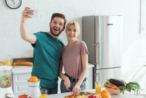 smiling vegan couple taking selfie while cooking together in kitchen at home - Photo, Image