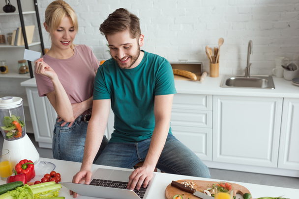 pareja vegana con portátil comprar bienes en línea juntos en la cocina en casa
 - Foto, Imagen