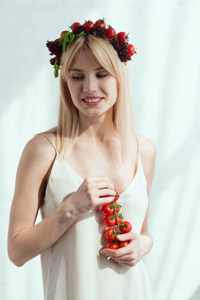 Lachende vrouw met cherrytomaatjes in handen en krans gemaakt van verse sla, cherrytomaatjes en veganistische levensstijl concept - Foto, afbeelding