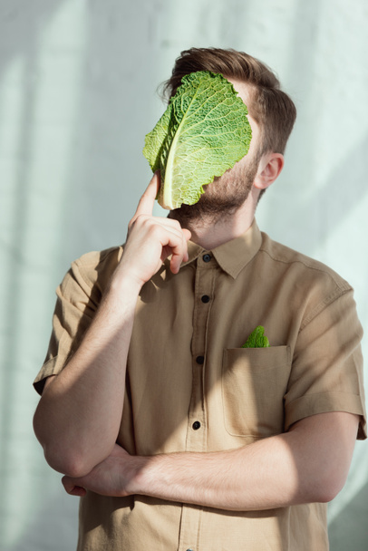 κρυμμένη άποψη συλλογισμένος άνδρα με φύλλα λάχανο Σαβοΐας στο πρόσωπο, ιδέα του τρόπου ζωής για χορτοφάγους - Φωτογραφία, εικόνα