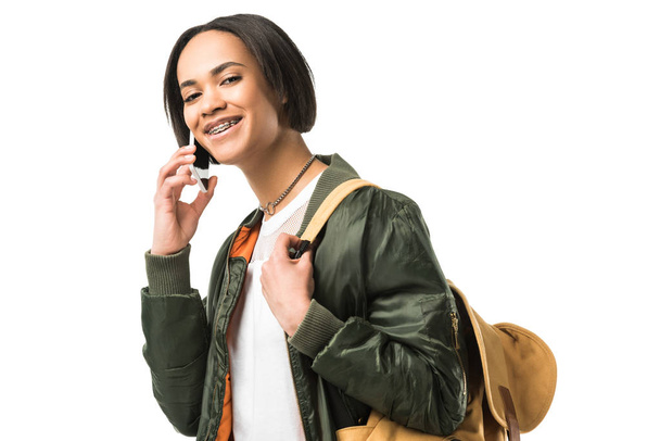 mutlu kadın Afrikalı-Amerikalı öğrenci ile smartphone, üzerinde beyaz izole konuşurken sırt çantası - Fotoğraf, Görsel