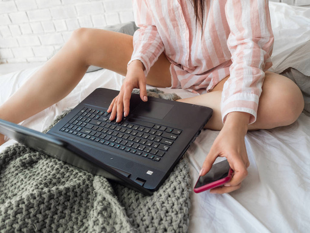 nő használ mozgatható telefon-val számítógép notebook ágyon - Fotó, kép