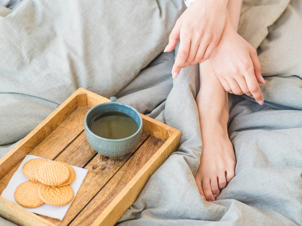 καφέ στο κρεβάτι. σχηματοποιημένα γυναικεία πόδια σε ζεστές κάλτσες, ξύλινο δίσκο για πρωινό στο κρεβάτι. Δύο φλιτζάνια καφέ και ζαχαρωτά. την έννοια του άνετου σπιτιού. πάνω όψη - Φωτογραφία, εικόνα
