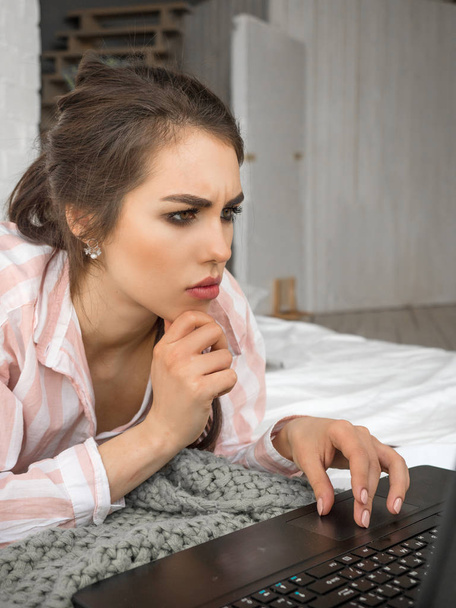 Chica adolescente grave acostado en la cama y el uso de la computadora portátil en casa
. - Foto, imagen