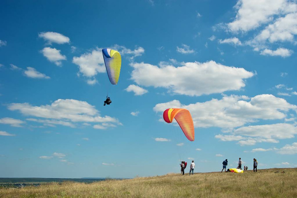 Des gens au sommet d'une colline se préparent à sauter en parachute. Un parachutiste déjà en l'air. Ciel nuageux en arrière-plan
.  - Photo, image