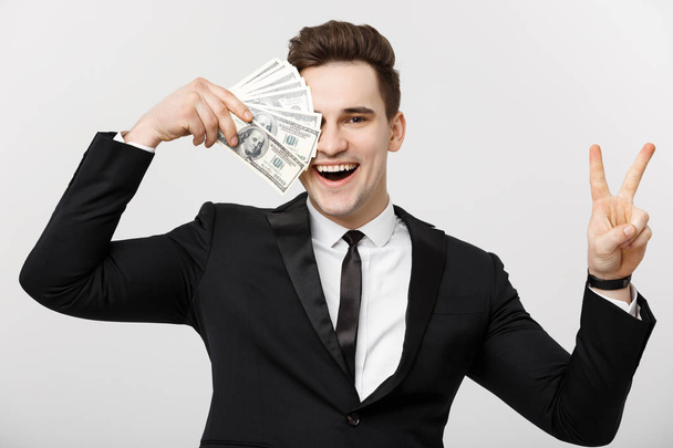 Πορτρέτο της ένας επιτυχημένος άνδρας αυτοπεποίθηση δείχνοντας μάτσο χρήματα τραπεζογραμματίων και δείχνει το σήμα της νίκης το δάχτυλό απομονωθεί σε λευκό φόντο - Φωτογραφία, εικόνα