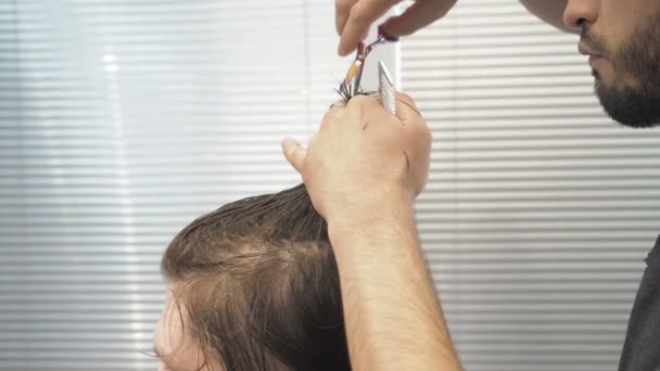 Перукар розрізає волосся зверху голови на клієнта в салоні. Чоловік сидить у кріслі перукарів під час стрижки з ножицями в перукарні
. - Кадри, відео