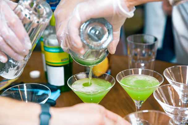 Barkeeper gießen ein fertiges alkoholisches Getränk in das Martini-Cocktailglas auf der Theke - Foto, Bild