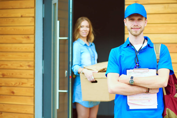 Smiling delivery man in blue uniform delivering parcel box to recipient - courier service concept. Smiling delivery man in blue uniform - Valokuva, kuva