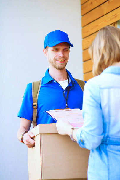 Smiling delivery man in blue uniform delivering parcel box to recipient - courier service concept. Smiling delivery man in blue uniform - Foto, Bild