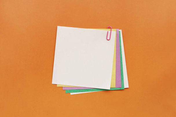A lot of colored paper fastened pink paperclip on orange background - Foto, Bild