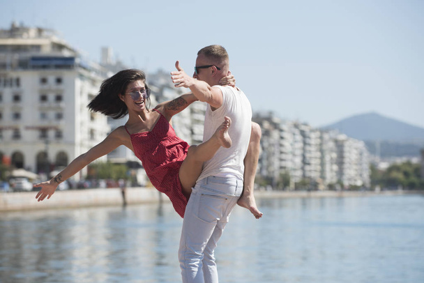 Happy family spend time together, dancing, having fun, sea and urban background. Couple in love stand on seafront. Family vacation concept. Man carries woman, couple on smiling faces. Love concept. - Fotó, kép