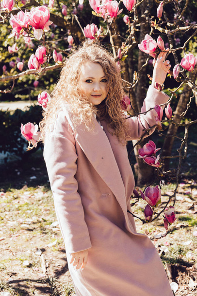 beautiful curly girl in a trendy pink coat walking in the park on a warm sunny day, smiling - Fotografie, Obrázek
