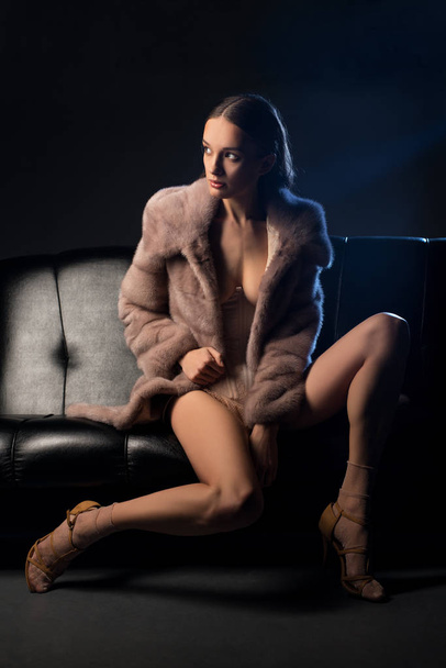 Pretty brunette in fur coat on a sofa in the dark - Foto, imagen