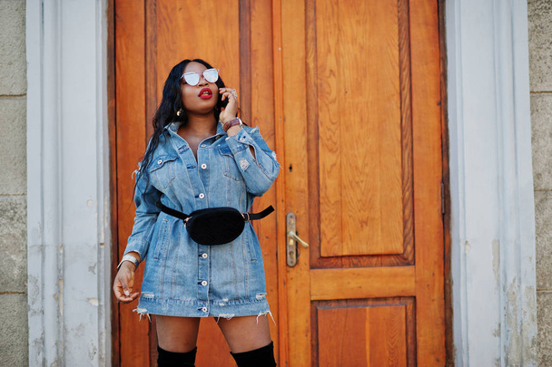 Африканская американка в джинсовом платье и солнцезащитных очках говорит о
  - Фото, изображение