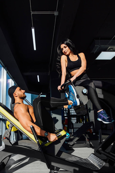 Personal trainer helping a men working out on leg press machine in gym - Photo, Image