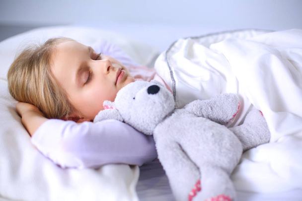 Child little girl sleeps in the bed with a toy teddy bear - Foto, imagen