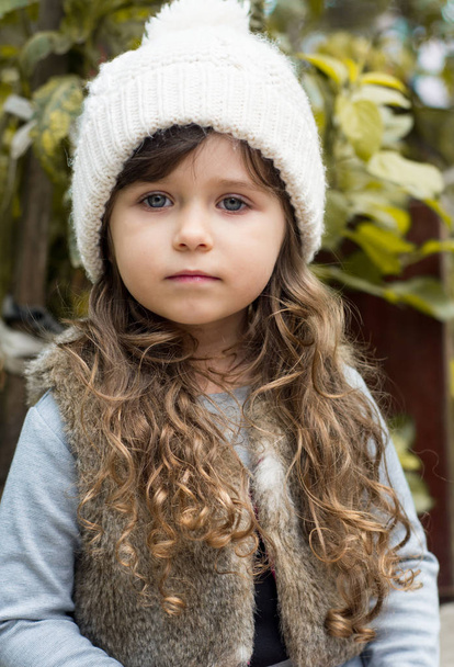 Beautiful little brunette girl, blue eyes. Outdoor portrait of a cute little 4 year old child wearing cap, autumn - Photo, Image
