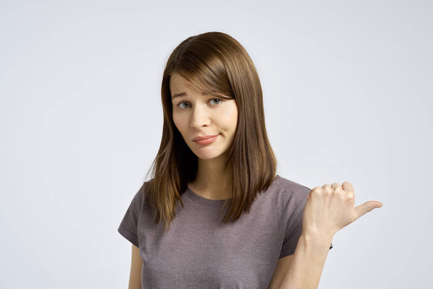 Studio portret van een jonge vrouw toont ontevredenheid met de duim aan de zijkant met negatieve emoties.  - Foto, afbeelding